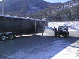 The trailer, parked next the the freeway at a truck stop, surrounded by patches of snow